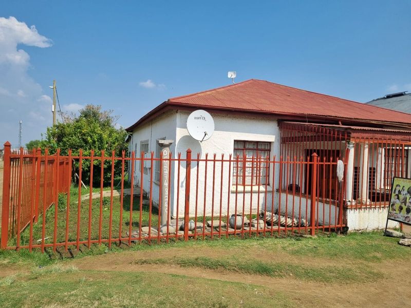 Front view of a single-story house featuring a corrugated metal roof, security fencing, and a concrete pillar entrance.