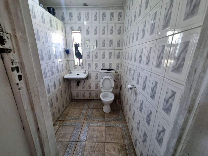 A compact bathroom featuring tiled walls and floors, equipped with a standard toilet and a wall-mounted basin.