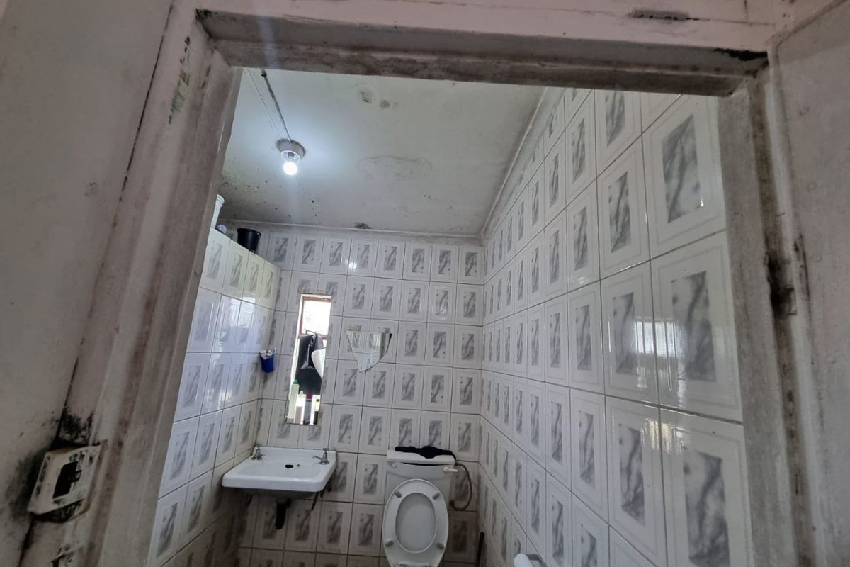 A small, dated bathroom featuring wall-mounted basin and toilet, requiring significant maintenance and cosmetic updates to the ceiling and finishes.