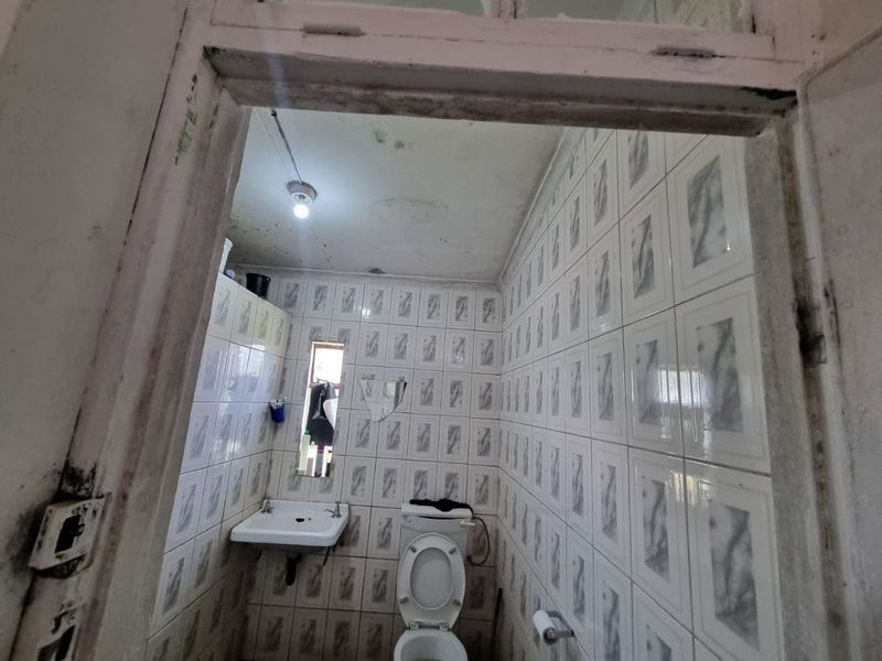 A small, dated bathroom featuring wall-mounted basin and toilet, requiring significant maintenance and cosmetic updates to the ceiling and finishes.