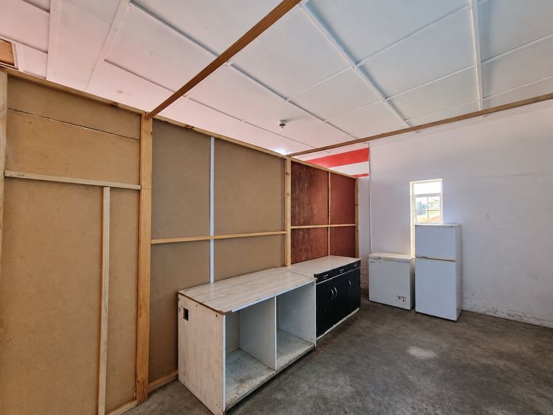 A utility or scullery area featuring basic built-in cabinetry, concrete flooring, and unfinished partition walls, offering potential for functional renovation.
