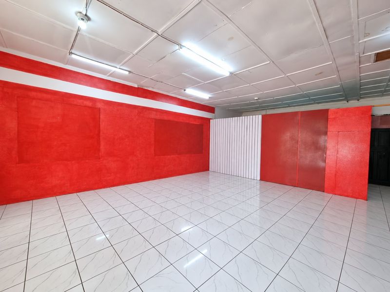 An empty, open-plan interior space featuring white tiled flooring, a suspended ceiling, and bold red wall finishes.