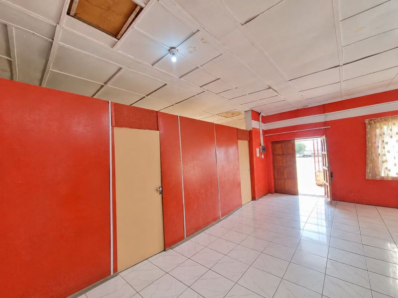 An empty living area featuring tiled flooring and a panelled ceiling, requiring cosmetic updates and ceiling repairs.