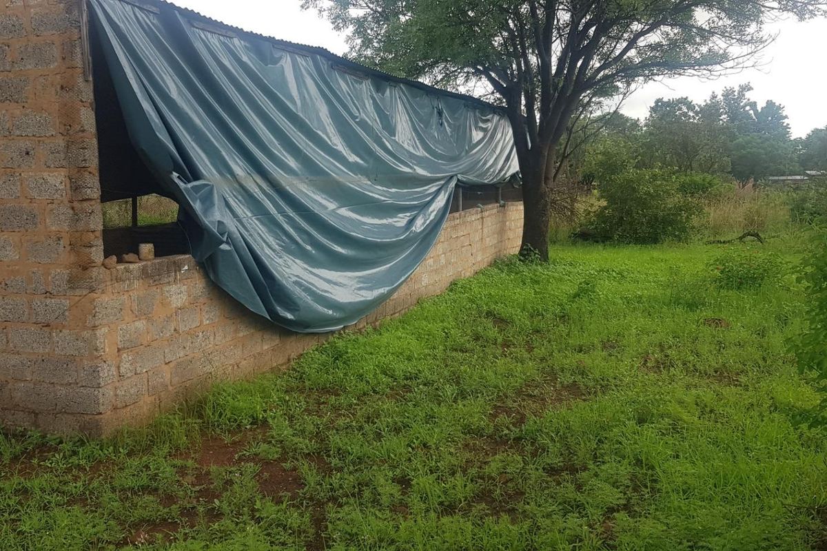 A basic utility structure constructed from cinder blocks with a corrugated metal roof, currently partially covered by a makeshift tarp.