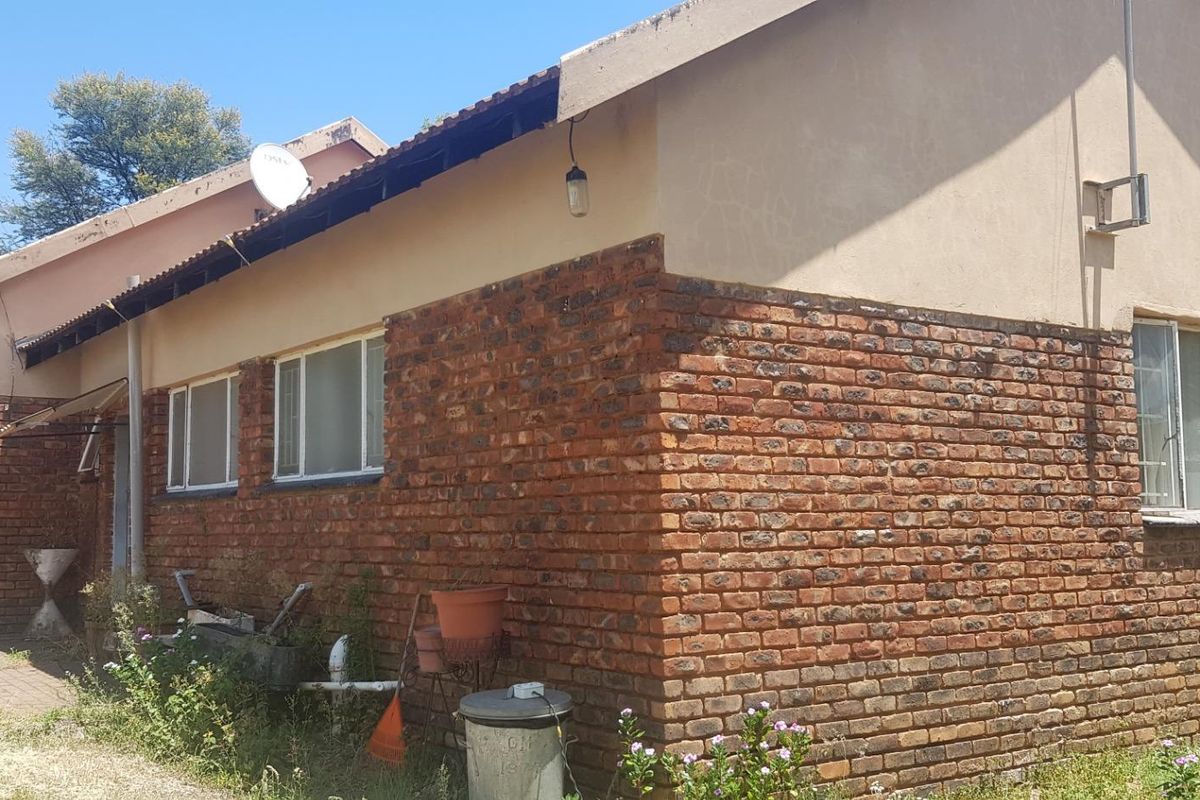 Rear view of a farm-style dwelling featuring exposed brickwork, metal window frames, and a tiled roof, requiring maintenance to the fascia and exterior finishes.