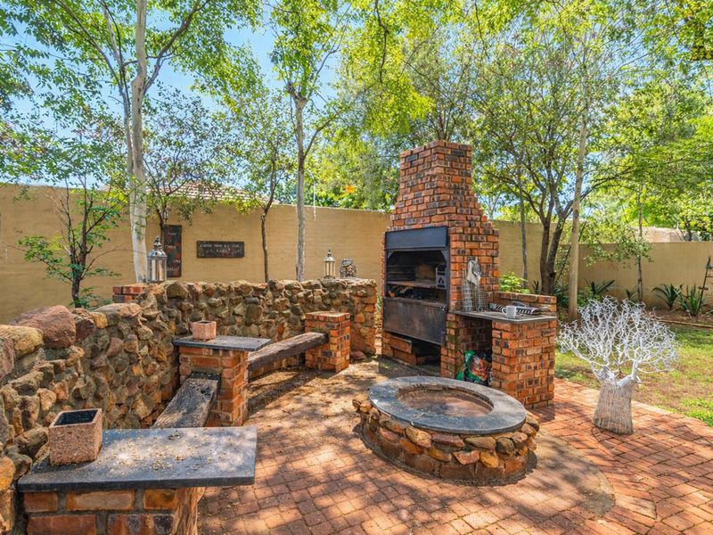 Outdoor entertainment area featuring a built-in brick braai, stone masonry seating wall, and a circular stone fire pit set on brick paving.