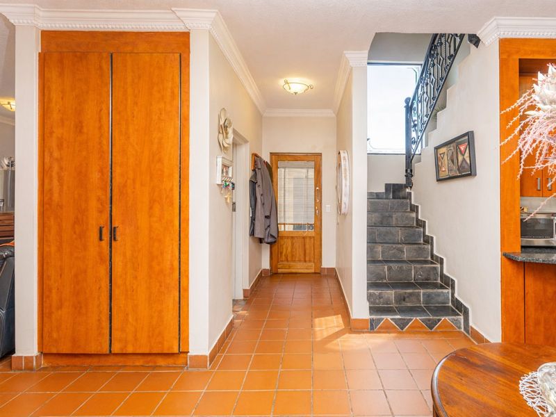 A spacious entrance hallway featuring terracotta tiled flooring, built-in wooden cabinetry, and a staircase with a decorative wrought iron balustrade.