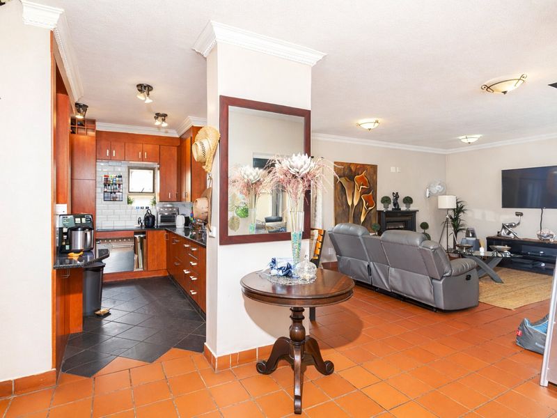 Open-plan living area featuring a kitchen with wood cabinetry, granite countertops, and terracotta flooring, seamlessly flowing into the adjacent living space.