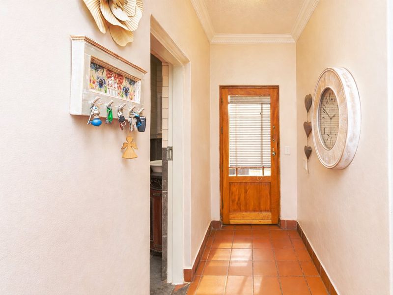 A bright hallway featuring terracotta floor tiles, crown molding, and a solid wooden door leading to an adjacent room.