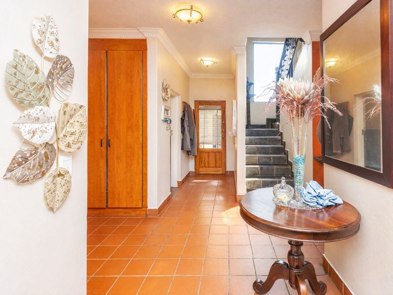 A welcoming entrance hall featuring terracotta tiled flooring, built-in wooden storage cabinetry, and a staircase leading to the upper level.