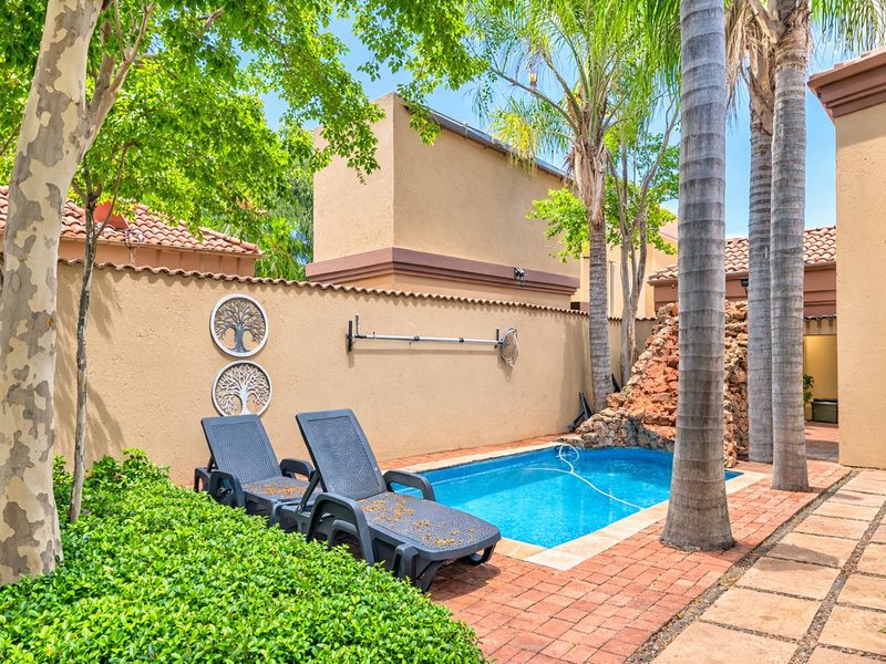 A private outdoor pool area featuring a rock water feature, brick paving, and established trees within a walled courtyard setting.