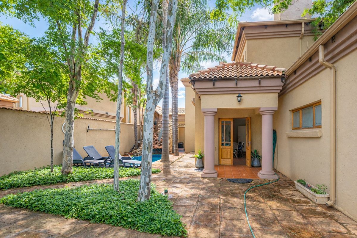 Rear exterior view featuring a covered patio entrance, a swimming pool, and a landscaped garden area with mature trees.