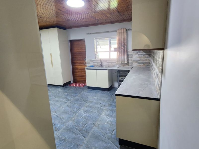 A clean, functional kitchen featuring modern cabinetry, stone-look countertops, tiled flooring, and a distinctive timber-paneled ceiling.