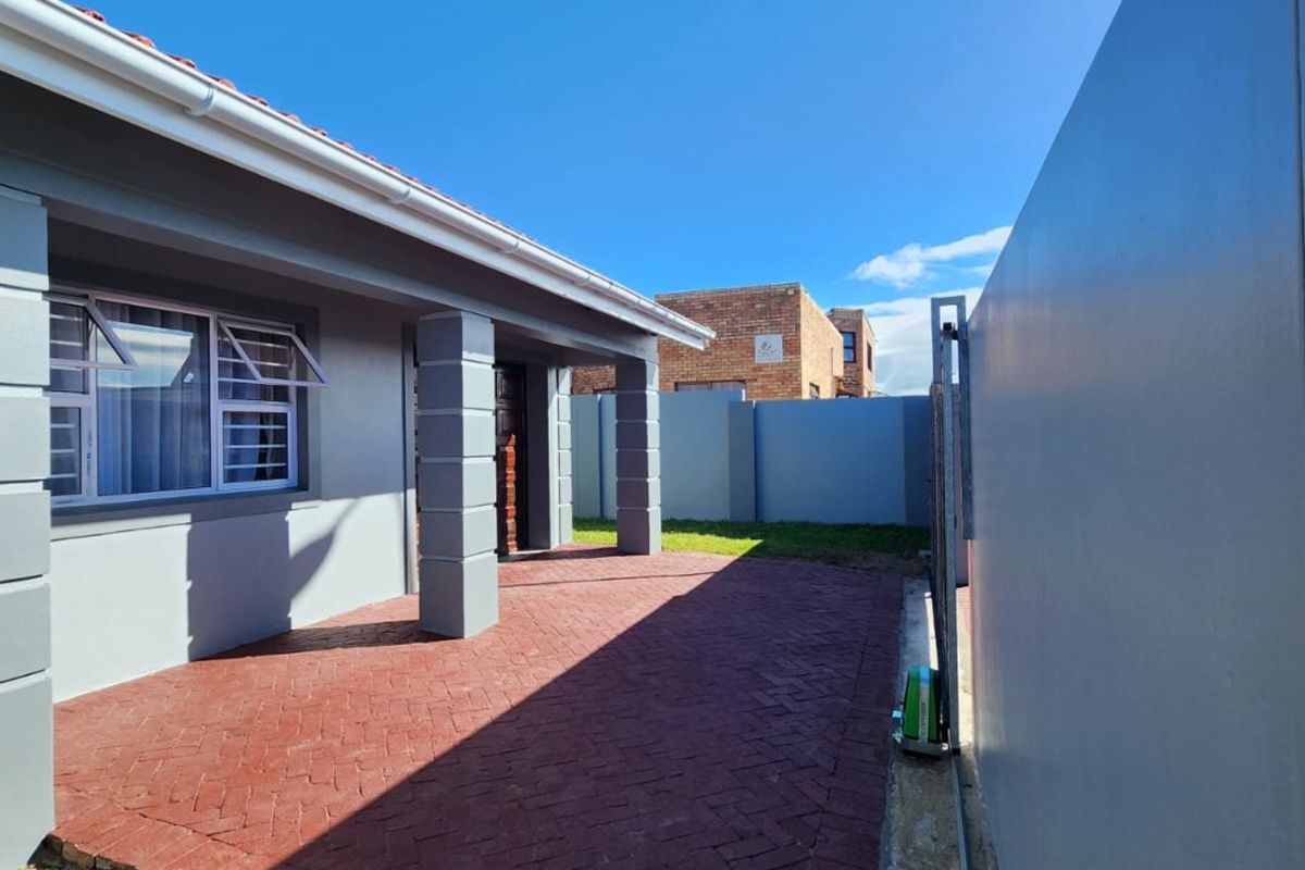 A well-maintained rear exterior view featuring a paved patio area, perimeter walling, and a sliding gate, providing a clean and secure outdoor space.