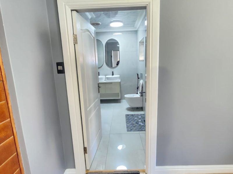 A view through a doorway into a modern bathroom featuring a double vanity, wall-mounted toilet, and sleek tiled finishes.