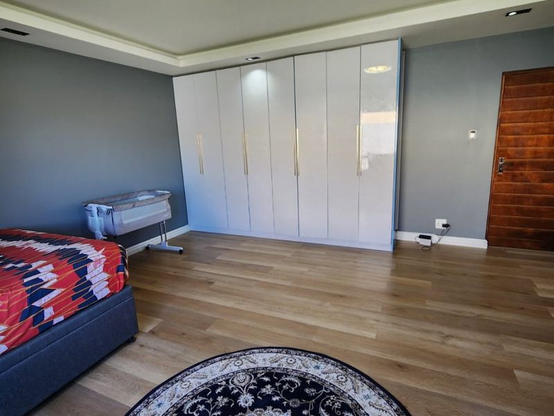 Spacious bedroom featuring modern laminate flooring, extensive built-in white cabinetry with gold handles, and recessed ceiling lighting.
