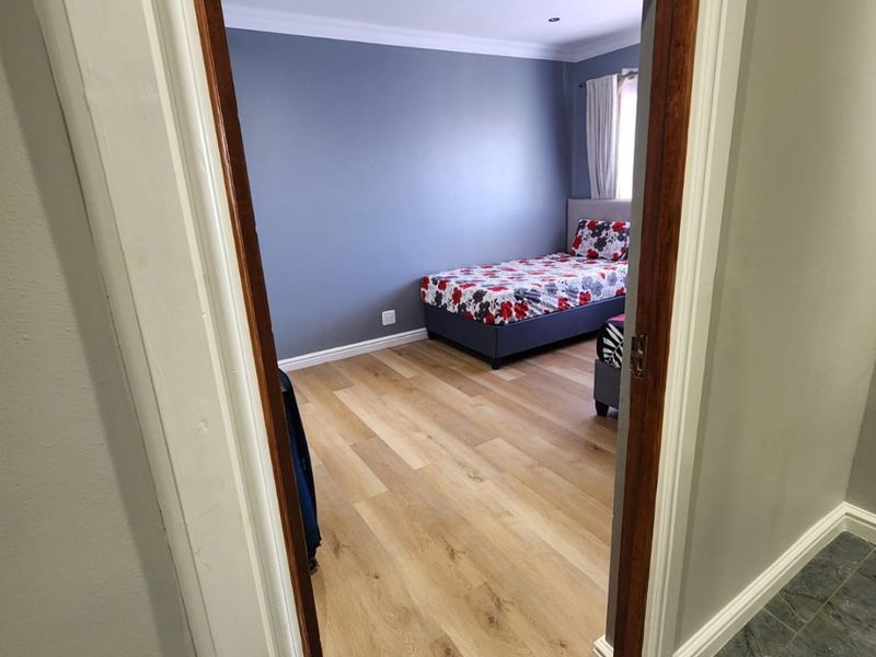 A well-maintained bedroom featuring modern laminate flooring, recessed downlighting, and decorative coving, viewed from the adjacent hallway.