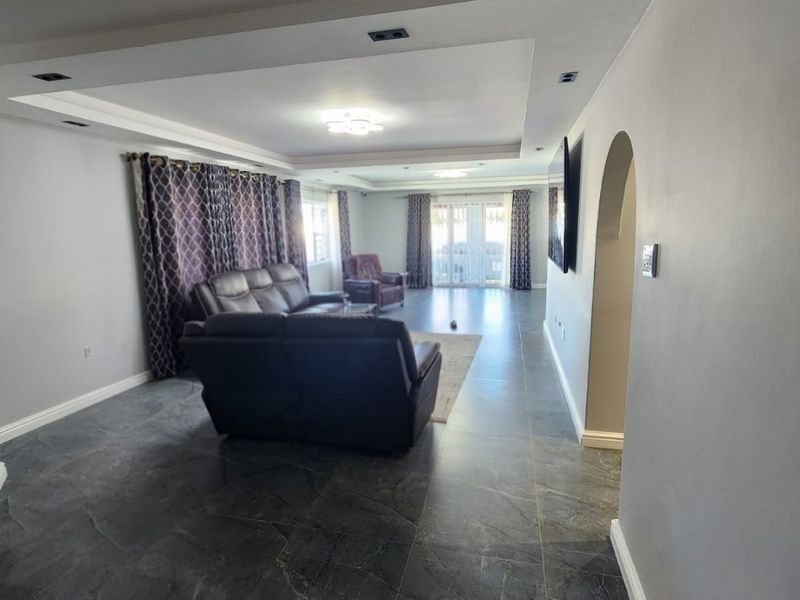 Spacious living room featuring a tray ceiling with recessed lighting, dark tiled flooring, and an elegant archway leading to adjacent areas.