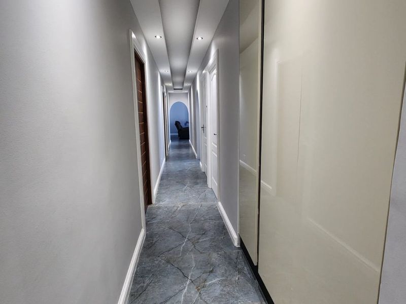 A modern, well-lit hallway featuring sleek marble-effect floor tiles and integrated floor-to-ceiling cabinetry, creating a clean and contemporary transition space.