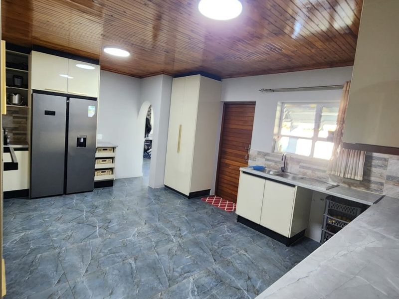 A functional kitchen featuring modern tiled flooring, built-in cabinetry, laminate countertops, and a distinctive timber tongue and groove ceiling.