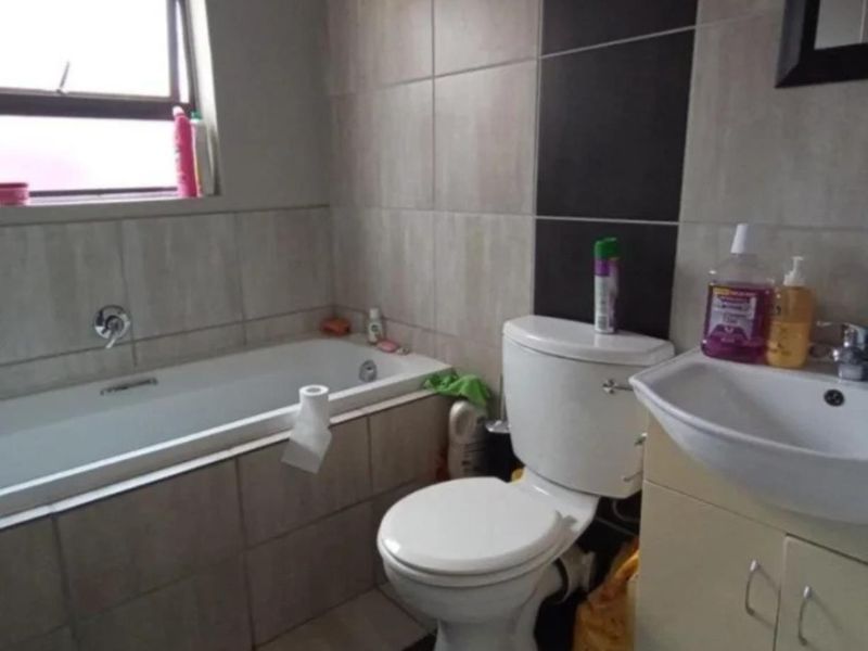 A functional bathroom featuring a bathtub, toilet, and vanity basin with neutral wall tiling and a window for natural light.