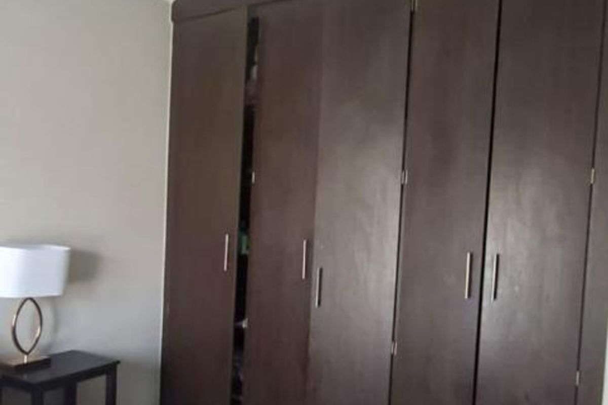 A bedroom featuring dark wood built-in cupboards and tiled flooring.