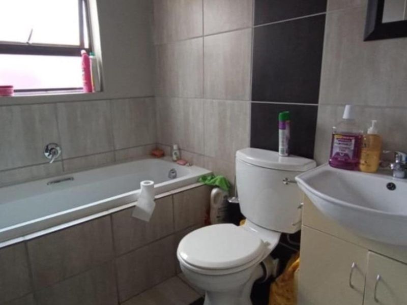 A functional bathroom featuring a bathtub, toilet, and vanity basin with neutral wall and floor tiling.