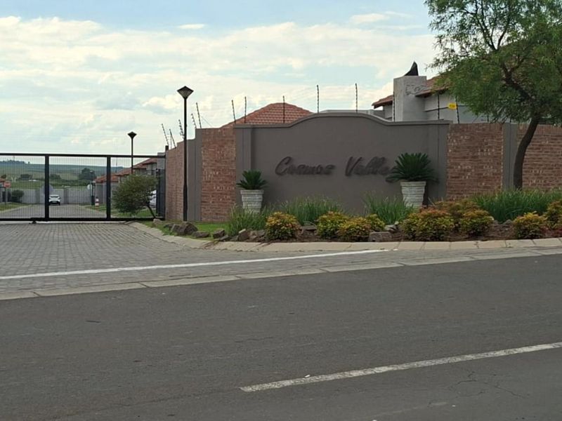 The entrance to Cosmos Valley estate featuring a secure gated access point, brick boundary walls with electric fencing, and paved driveway.