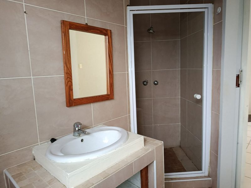 A functional bathroom featuring a tiled shower enclosure, a vanity basin with a mixer tap, and wall-mounted mirror.