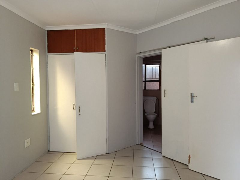 An empty bedroom featuring tiled flooring, built-in cupboards, and direct access to an en-suite bathroom.