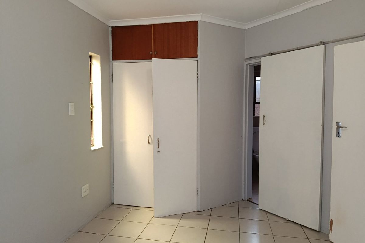 An empty bedroom featuring tiled flooring, built-in cupboards with overhead storage, and a sliding door leading to an adjacent space.