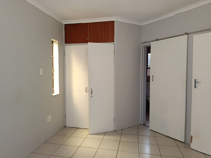 An empty bedroom featuring tiled flooring, built-in cupboards with overhead storage, and a sliding door leading to an adjacent space.