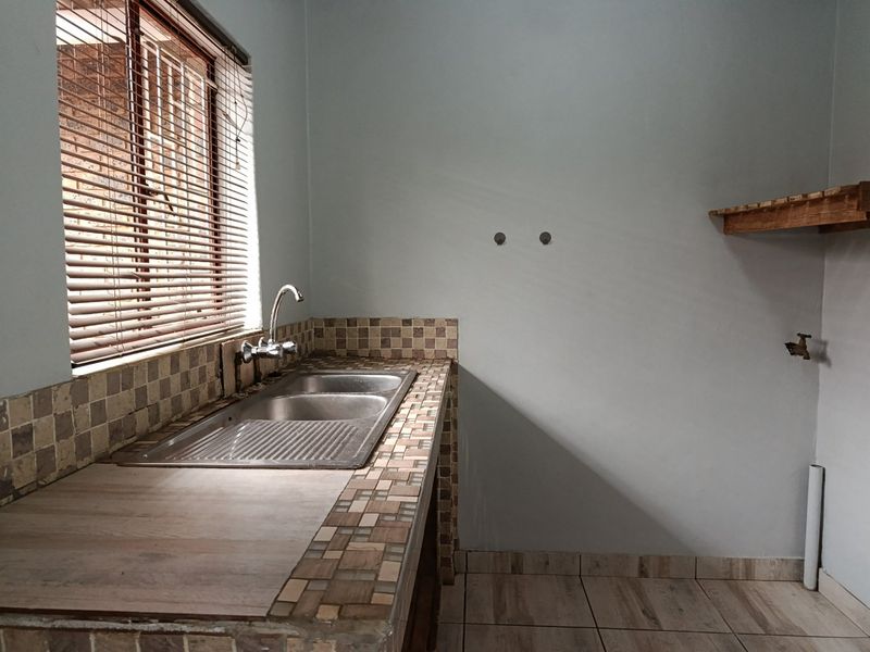 A functional laundry area featuring a double bowl stainless steel sink, tiled splashback, and dedicated plumbing connections for appliances.