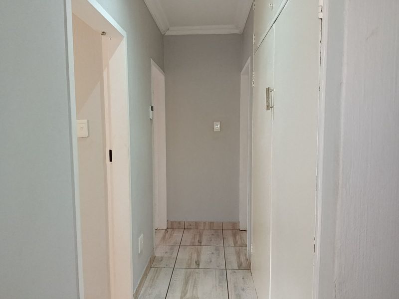 A clean, neutral hallway featuring tiled flooring and built-in storage cupboards, providing efficient access to adjacent rooms.