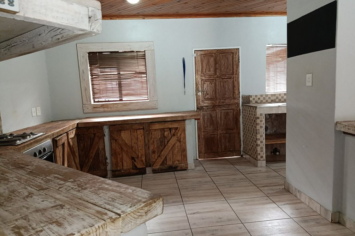 A rustic kitchen featuring wooden cabinetry, tiled flooring, and a timber ceiling, offering a dated aesthetic with potential for modernization.
