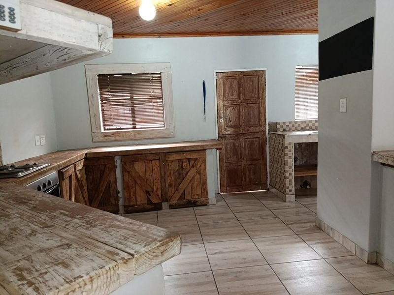 A rustic kitchen featuring wooden cabinetry, tiled flooring, and a timber ceiling, offering a dated aesthetic with potential for modernization.