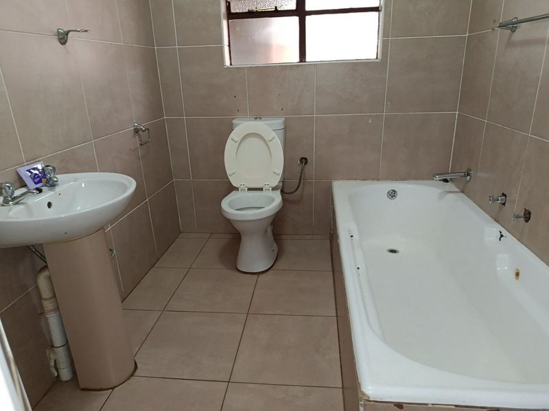 A functional bathroom featuring a pedestal basin, toilet, and bathtub with full-height wall tiling and a window for natural light.