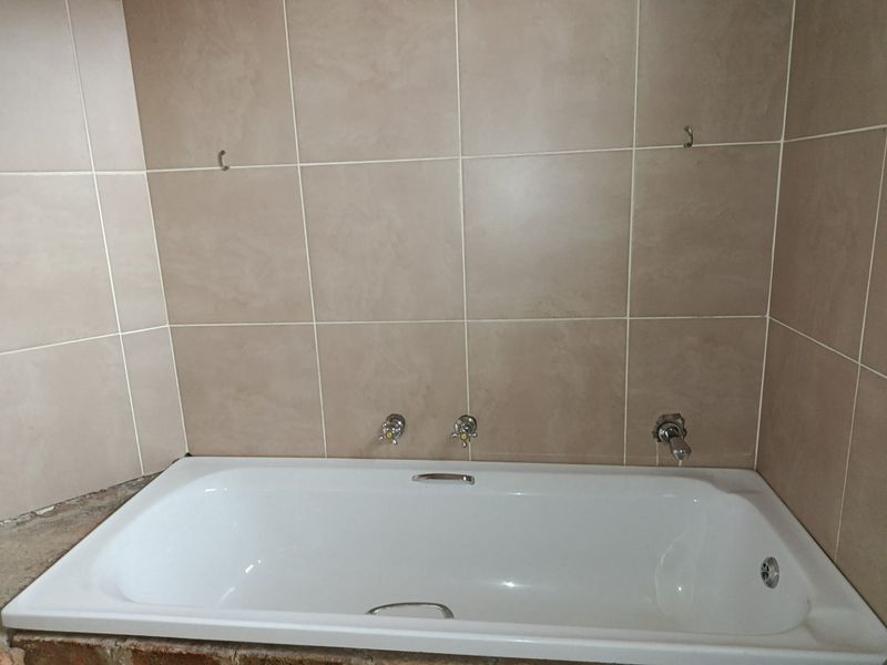 A bathroom featuring a built-in bathtub with wall-mounted taps and tiled surround, currently requiring finishing touches to the base and edges.
