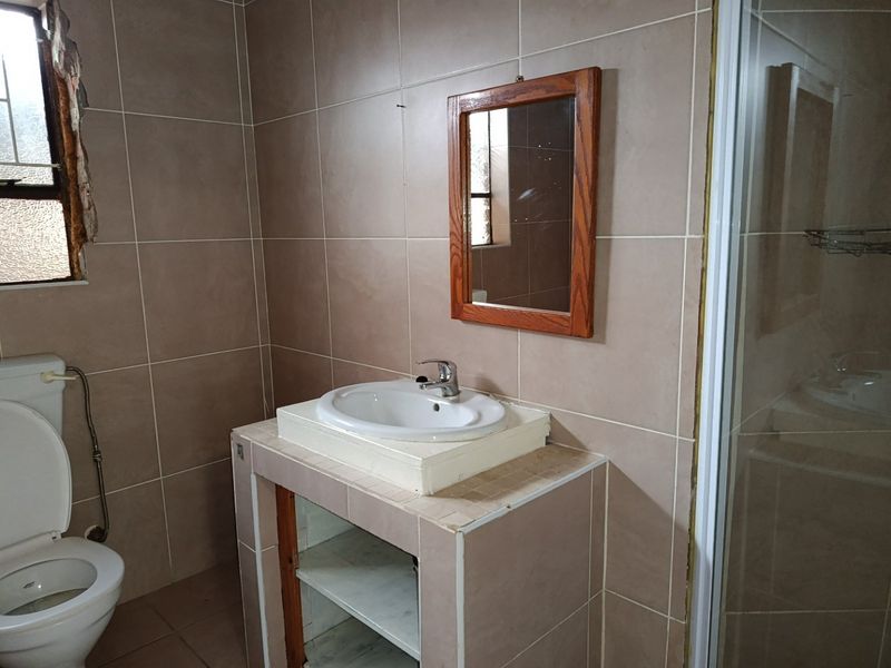 A bathroom featuring tiled walls and flooring, a built-in vanity with a ceramic basin, a toilet, and a shower enclosure.