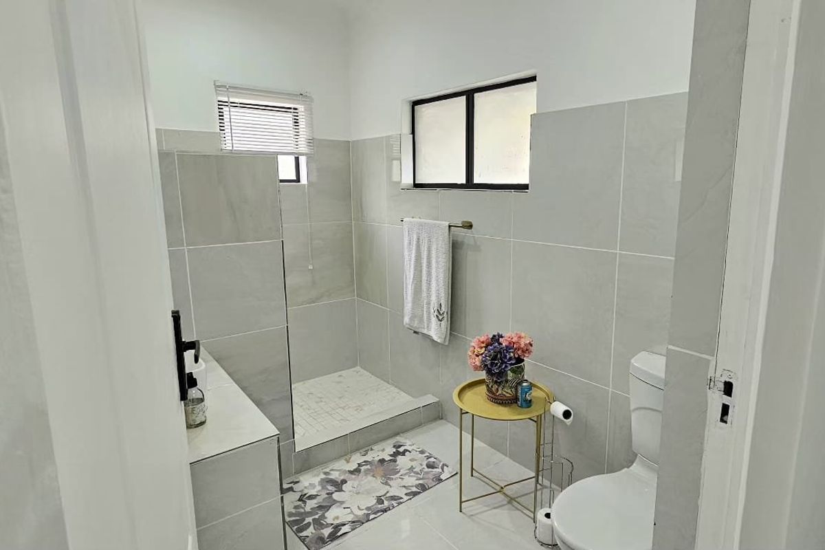 A modern bathroom featuring neutral grey wall and floor tiles, a walk-in shower enclosure, and a standard toilet.