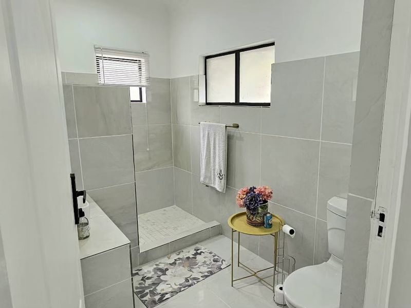 A modern bathroom featuring neutral grey wall and floor tiles, a walk-in shower enclosure, and a standard toilet.