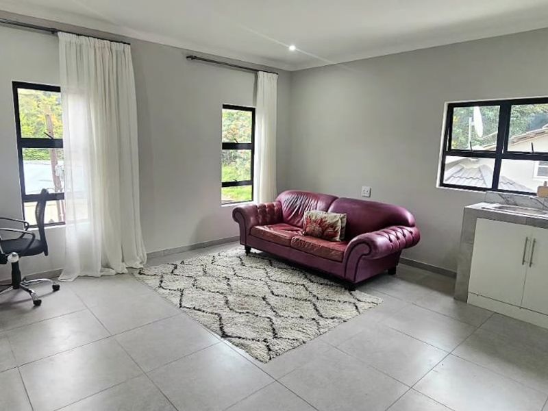 An open-plan living area featuring tiled floors, neutral walls, and a compact kitchenette with built-in cabinetry and a sink.