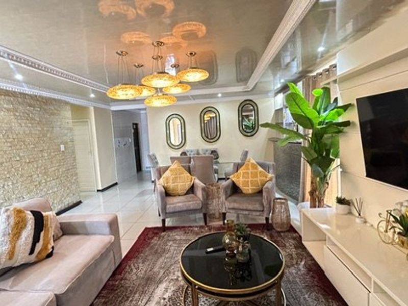 Spacious living room featuring a textured stone accent wall, glossy ceiling with decorative molding, and polished floor tiles.