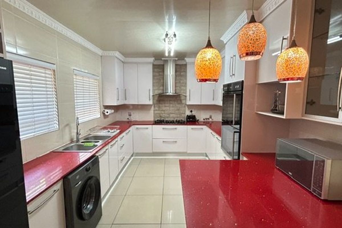 Modern kitchen featuring white cabinetry, striking red stone countertops, integrated appliances, tiled flooring, and decorative coving.