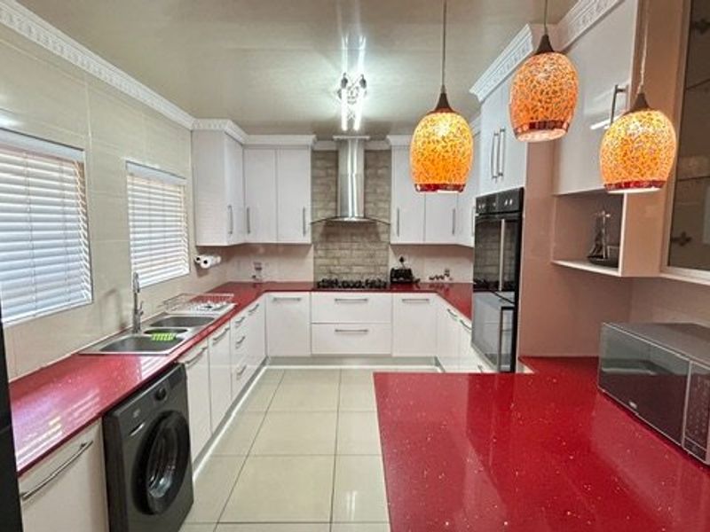 Modern kitchen featuring white cabinetry, striking red stone countertops, integrated appliances, tiled flooring, and decorative coving.