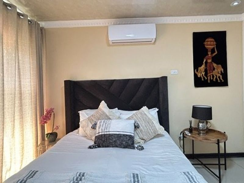 A well-maintained bedroom featuring a split-system air conditioner, built-in wardrobe, crown molding, and tiled flooring.