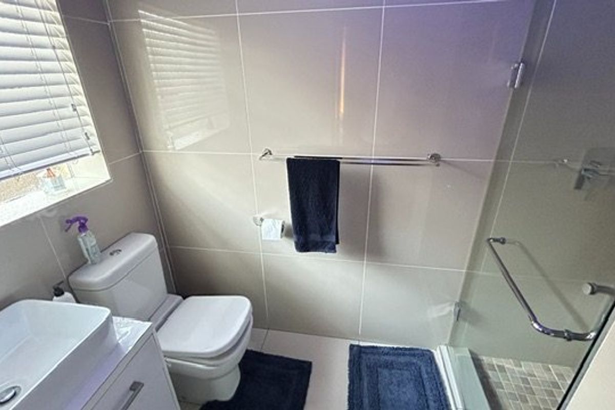 Modern bathroom featuring a vessel sink vanity, a glass-enclosed shower with tiled finishes, and a window with venetian blinds.