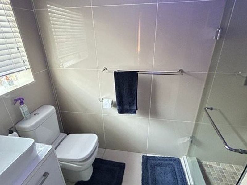 Modern bathroom featuring a vessel sink vanity, a glass-enclosed shower with tiled finishes, and a window with venetian blinds.