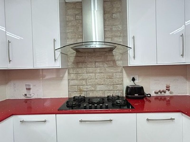 Modern kitchen featuring white gloss cabinetry, striking red quartz countertops, a gas hob, and a stylish brick-effect splashback with integrated extractor fan.