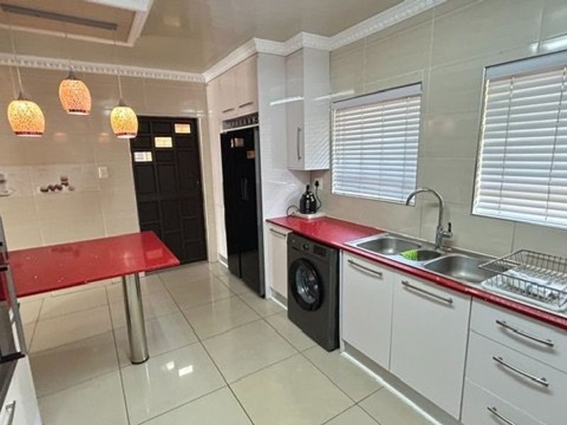 A well-maintained kitchen featuring red countertops, built-in oven, double sink, tiled flooring, and ample cabinetry with modern finishes.